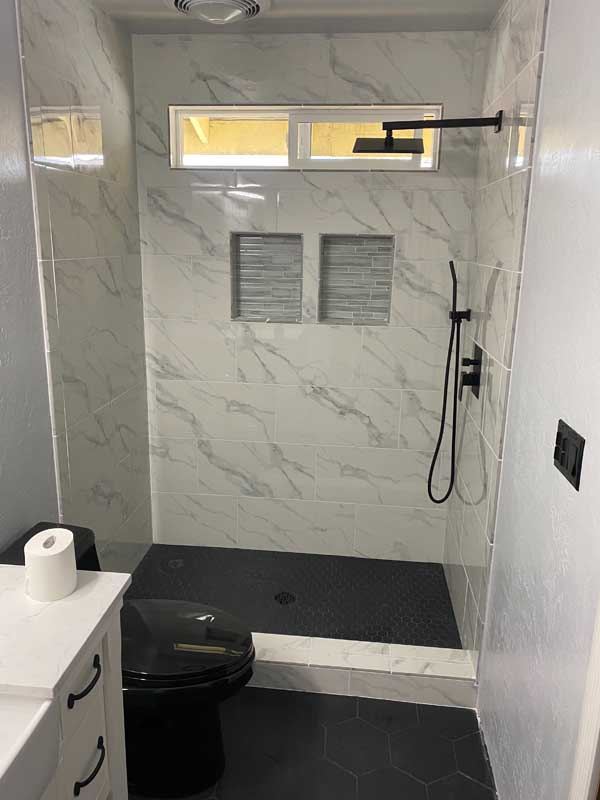 The finished shower in white marble-look tile above a dark tiled floor.