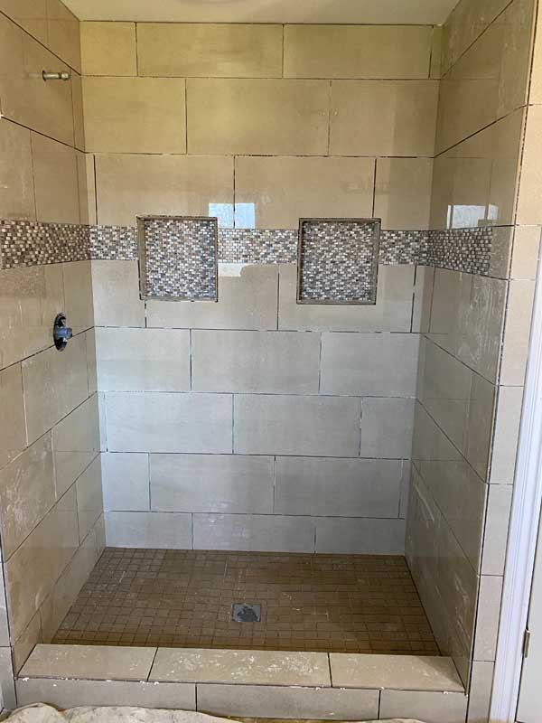 The finished shower in cream stone-look tile with inset accent squares.