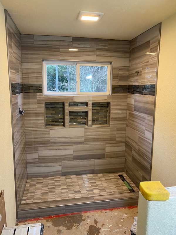 The finished walk-in shower in wood-look plank tile wrapping the window.