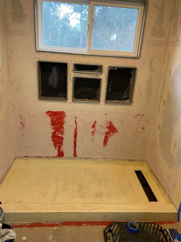 Framed shower pan with red waterproofing applied and bare walls.