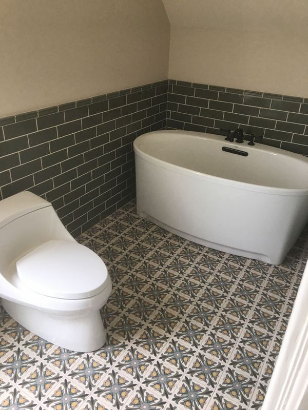 Patterned encaustic-look floor tile running under a freestanding tub with tiled wainscot.