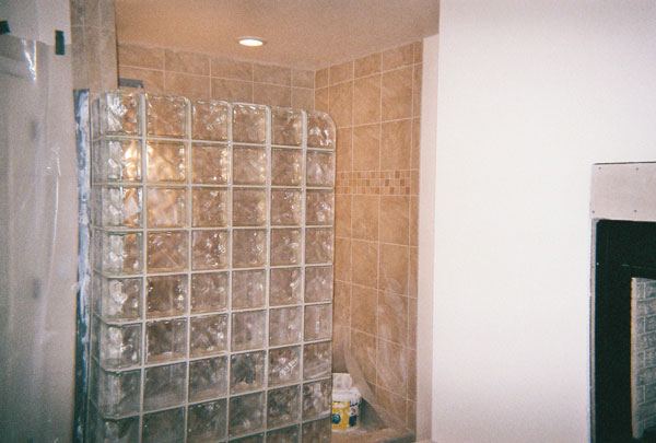 Glass-block shower wall beside travertine tile.