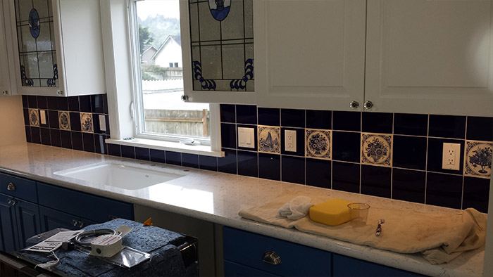 Kitchen backsplash in cobalt and hand-painted decorative tile beneath a stained-glass window.