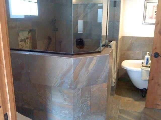 Bathroom with a copper-toned slate shower surround beside a freestanding clawfoot tub.